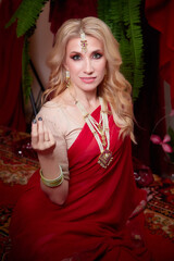 A beautiful European girl looking like an Arab woman in a red room in a harem. Photo shoot of an oriental style odalisque. A model poses in a sari as an indian woman in india