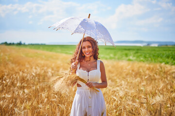 A beautiful woman on a sunny day with an umbrella in a field.