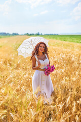A beautiful woman on a sunny day with an umbrella in a field.