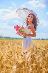 A beautiful woman on a sunny day with an umbrella in a field.
