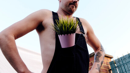 Man with plant in bib overalls at back yard