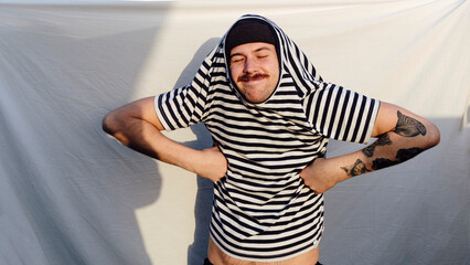 Smiling man wearing striped t-shirt with arms akimbo standing in front of white backdrop