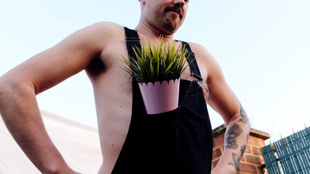 Man With Plant In Bib Overalls At Back Yard