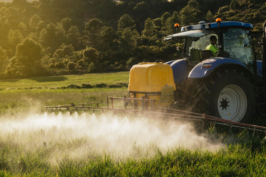 Farmer spraying fertilizer through sprayer on tractor on field