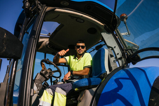 Farmer wearing sunglasses gesturing thumbs up sitting in tractor