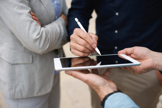 Hand of businessman signing on tablet PC standing by colleagues