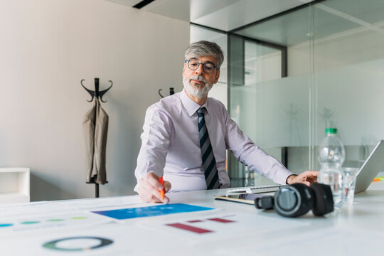 Businessman wearing eyeglasses analyzing chart in office - Powered by Adobe