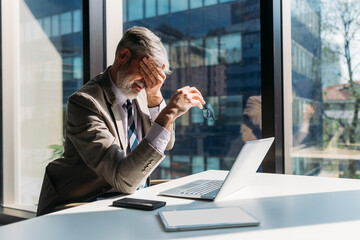 Tired businessman sitting with hand covering eye at desk in office