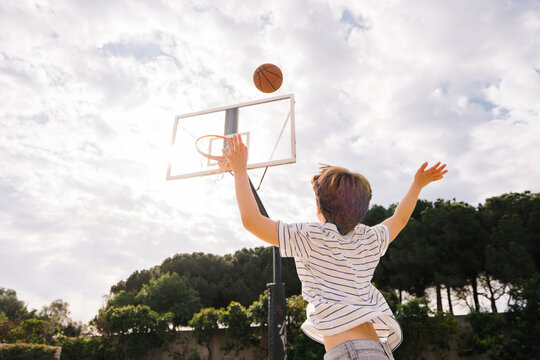 Boy throwing basketball at sports court on sunny day