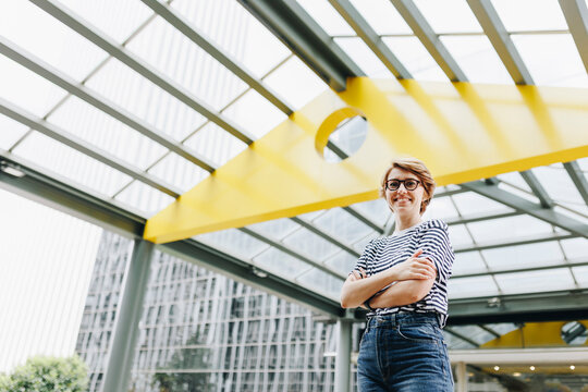 Smiling woman with arms crossed standing at office building entrance