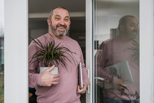 Happy businessman with dragon tree and laptop at office doorway