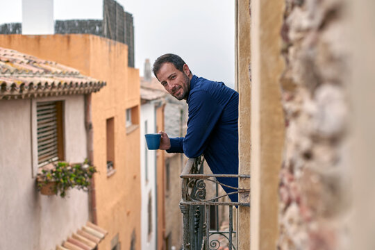 Smiling man with coffee cup leaning on railing of balcony