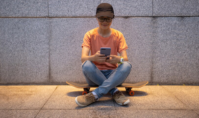 Female skateboarder using smartphone leaning on wall in city