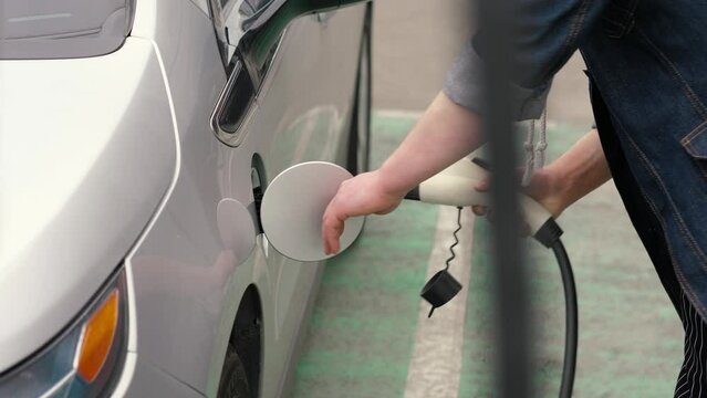 Male hand unplugs charging cable to electric vehicle and charges batteries. EV station in parking lot. Unrecognizable man disconnects power connector into EV car.