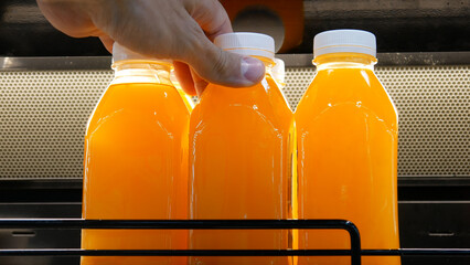 Close-up of plastic bottles with natural fruit juice on the fridge shelf and a male hand takes one