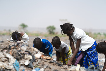 Four West African homeless children digging in a landfill looking after recyclable items to sell;...