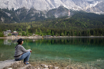 Fototapeta na wymiar Caucasian female sitting on a stone near the Eibsee Lake, Germany. Travel, lifestyle concept.
