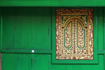 The Balinese carving wooden window on green wall.