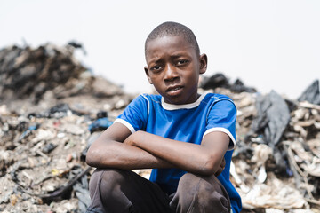 Pensive young african waste collector boy sitting tired on top of a pile of plastic trash in a...