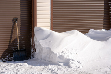 Covered by a snowdrift, garage doors on a bright, sunny day. Cleared of snow drift, shoveled gate on the right side..