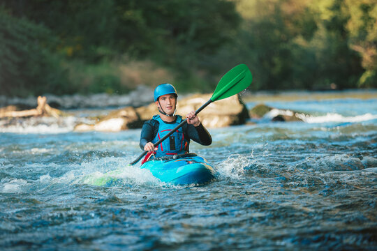 Male recreational athlete paddling carefully over the risky, foamy, and splashy whitewater rapids in his blue kayak