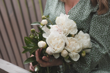 Hands of a woman in close-up with a bouquet of white peonies. Authenticity. Environmental friendliness. Content for a flower shop. Sale of flowers.