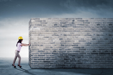 Female engineer pushing a big brick wall