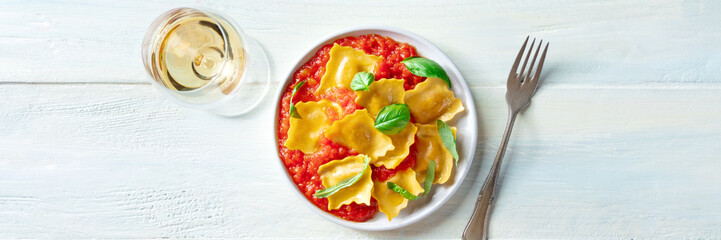 Ravioli with tomato sauce and basil with a glass of white wine, a panorama for an Italian restaurant menu, overhead flat lay shot