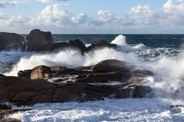Rough sea and big waves hit rocks creating enormous spray.