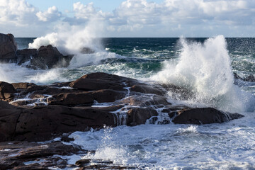 Rough sea and big waves hit rocks under friendly sky.