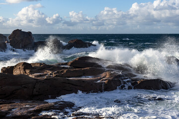 Rough sea and big waves hit rocks under friendly sky.