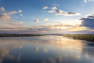 Evening landscape, sunset on the river. Wide river, horizon, clouds are reflected in the water.