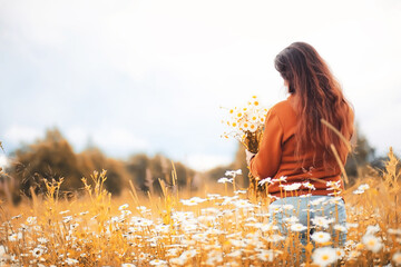 Beautiful girl collects daisies in autumn