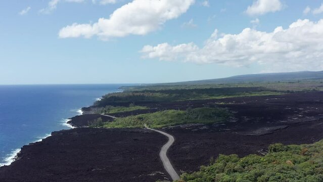 Wide aerial shot flying over a recently dried lava flow with a road cutting across it on the Big Island of Hawaii. 4K