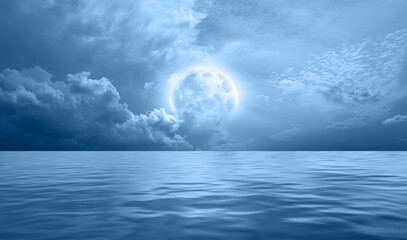 Night sky with blue moon in the clouds over the calm blue sea, many stars in the background ...