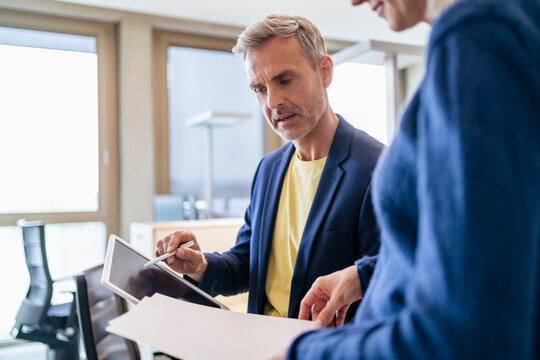 Businessman and businesswoman working together on digital tablet and papers in office