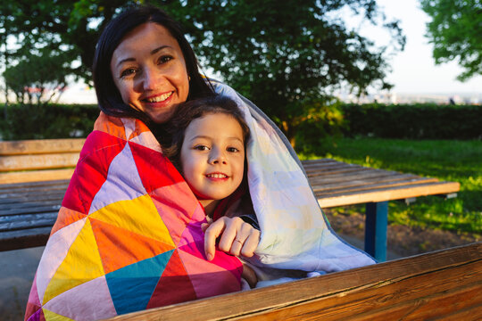 Happy mother and daughter wrapped in quilt blanket at park