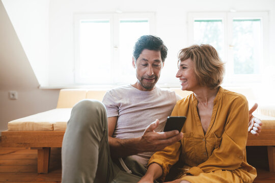 Happy woman looking at man using smart phone at home