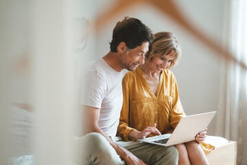 Happy woman using laptop sitting by man at home