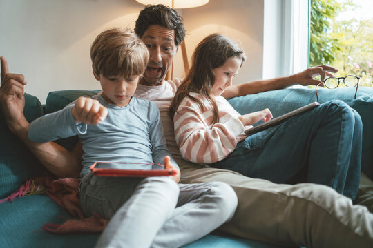 Happy father sitting with daughter and son using tablet PC at home
