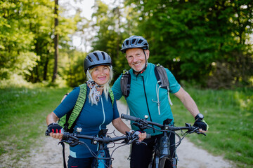 Portrait of active senior couple riding bicycles at summer park, standing on path and looking at...