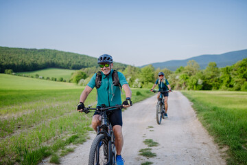 Obraz na płótnie Canvas Active senior couple riding electric bicycles on trail at summer park, healthy lifestyle concept.