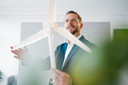 Happy businessman touching blade of windmill model in office