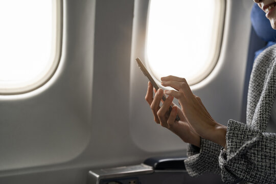 Side view of young businesswoman using smartphone in aircraft, hipster guy holding mobile device for playing or working during flight, business travel concept