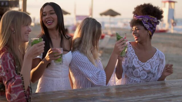 Young beautiful women drinking and dancing at cocktail party on the beach, female friends having fun at chiringuito during vacation, holiday activities, slow motion clip