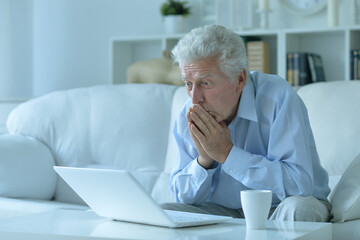 Fototapeta premium Emotional senior man using laptop at home