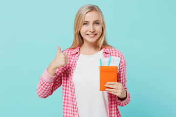 Traveler tourist woman in pink shirt hold passport boarding tickets show thumb up isolated on plain pastel light blue background Passenger travel abroad on weekends getaway Air flight journey concept