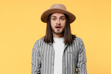 Young shocked surprised sad man he 20s wearing striped grey shirt white t-shirt hat look camera with opened mouth isolated on plain yellow color background studio portrait. People lifestyle concept.