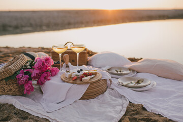 Beautiful romantic picnic with two glasses of white wine, fresh cheese and berries on the beach at...