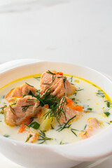 Norwegian red salmon fish soup with vegetables, herbs and cream, bowl of soup on a white marble background